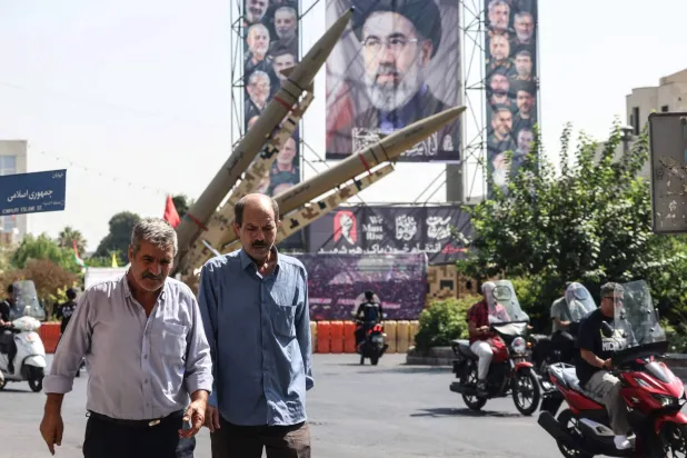 رجال إيرانيون يمرون بجوار صواريخ معروضة بجانب صورة كبيرة للمرشد الإيراني مجتبى خامنئي في ساحة بهارستان في طهران يوم 28 سبتمبر 2026 (أ.ف.ب) 