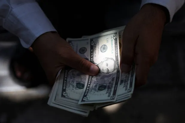 تاجر عملات يحمل أوراقًا نقدية من فئة الدولار الأميركي في طهران (رويترز)