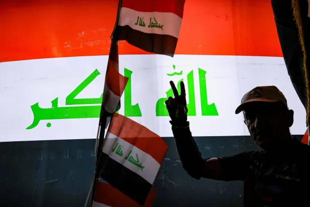 A man gestures in front of a display of the Iraqi flag while celebrating the withdrawal of US-led coalition forces from Iraq, ending a military presence that began after the 2003 US-led invasion, in Baghdad, Iraq, September 30, 2026. (Reuters) 