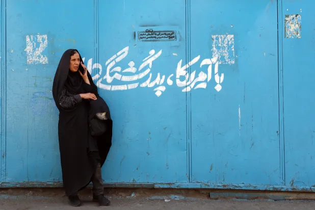 An Iranian woman stands next graffiti reading in Persian, “We have a blood feud with the US,” in a street in central Tehran, Iran, 13 September 2026. (EPA) 