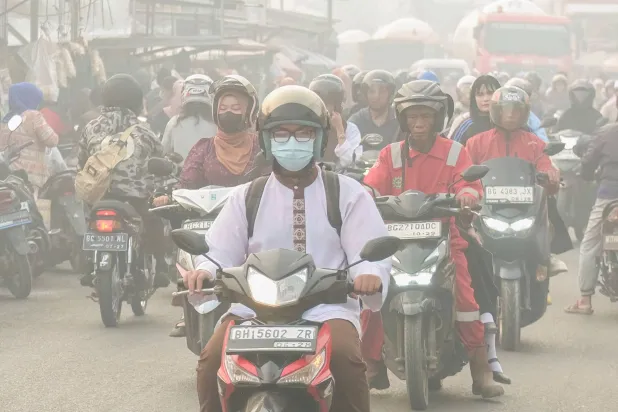 People commute along a road as haze from forest and land fires shrouds Palembang, South Sumatra on October 2, 2026. (Photo by AL ZULKIFLI / AFP)