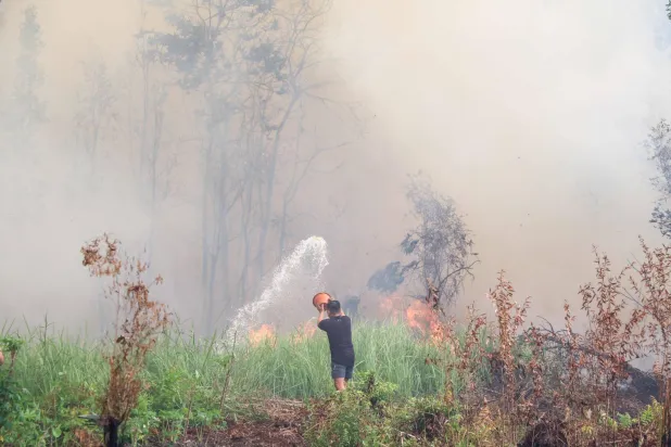 A man attempts to extinguish flames with a bucket amid thick smoke and fires burning through peatland in Palangkaraya, Central Kalimantan, on October 3, 2026. (Photo by REINA / AFP)