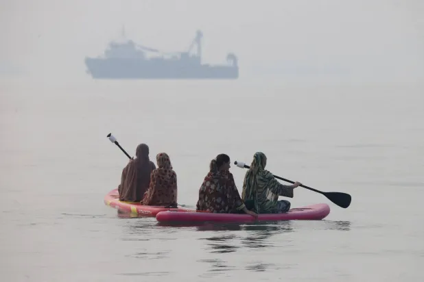 Women use paddleboards, as a vessel in the Strait of Hormuz appears in the distance, near the beach of Bandar Abbas, Iran, October 6, 2026. Amirhosein Khorgooi/ISNA/via WANA (West Asia News Agency) via REUTERS 