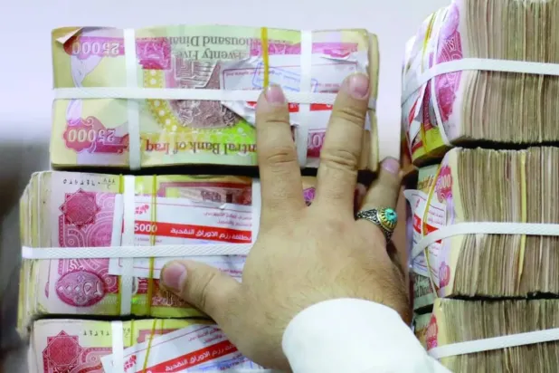 An employee arranges stacks of Iraqi dinars at a currency exchange shop in Baghdad on Feb. 14, 2023. (AFP)
