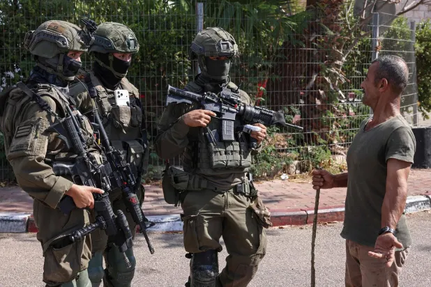 مزارع فلسطيني يتحدث مع جنود إسرائيليين خلال موسم الحصاد في كروم الزيتون الفلسطينية بقرية رنتس قرب رام الله في الضفة الغربية المحتلة (أ.ف.ب)