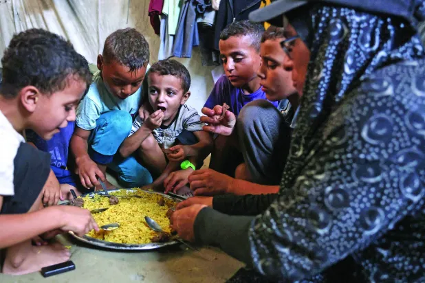 
نازحة فلسطينية من بيت حانون تتقاسم مع أطفالها طعاماً حصلت عليه من مطبخ خيري في خان يونس جنوب قطاع غزة أمس (أ.ف.ب)