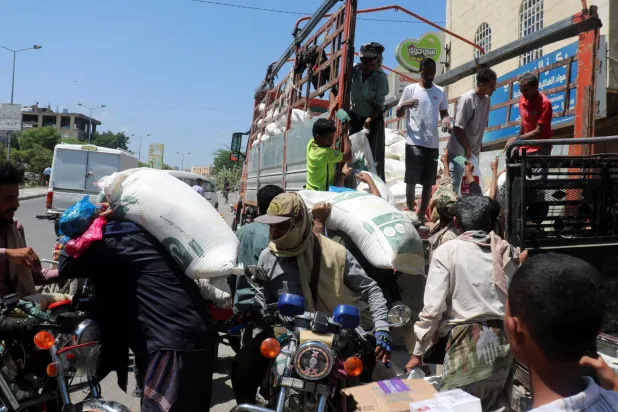 أشخاص ينقلون دقيق القمح من على متن شاحنة في تعز المحاصرة من قبل الحوثيين (رويترز)