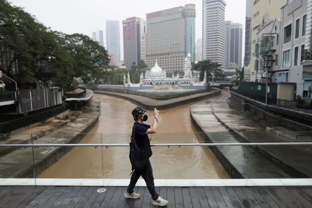 A man wearing a face mask takes a photo with his phone, with Kuala Lumpur’s skyline in the background shrouded in haze from regional wildfires, in Kuala Lumpur, Malaysia, October 15, 2026. REUTERS/Hasnoor Hussain