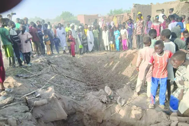 سودانيون يعاينون حفرة سببتها مُسيَّرة استهدفت في وقت سابق مخيماً للنازحين بوسط دارفور (الأمم المتحدة)