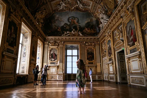 (FILES) Visitors take a picture of the window which was broken during the reopening to the public of the Apollo Gallery, where French crown jewels worth 88 million euros were stolen in 2025 in a brazen heist, at the Musée du Louvre in Paris on July 22, 2026. (Photo by LOU BENOIST / POOL / AFP)