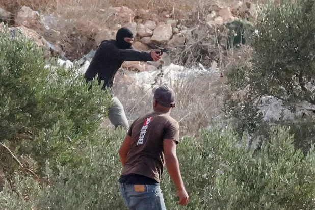 An Israeli settler points a gun amid clashes with Palestinians harvesting olives in Abu Falah near Ramallah in the Israeli-occupied West Bank, October 16, 2026. (Reuters)