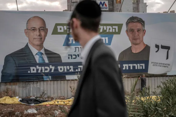 An ultra-Orthodox Jewish man walks past an electoral banner for the Reservist party's list led by Yoaz Hendel (R) and Yaron Zelekha (L) in Bnei Barak near Tel Aviv on October 18, 2026. (Photo by Ilia YEFIMOVICH / AFP)