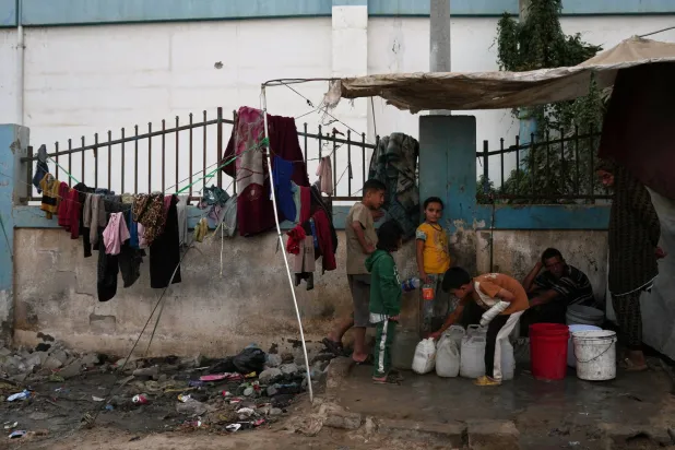 Palestinians fill plastic bottles with water at a tent camp in Deir al-Balah, Gaza Strip, Thursday, Oct. 22, 2026. (AP Photo/Abdel Kareem Hana)