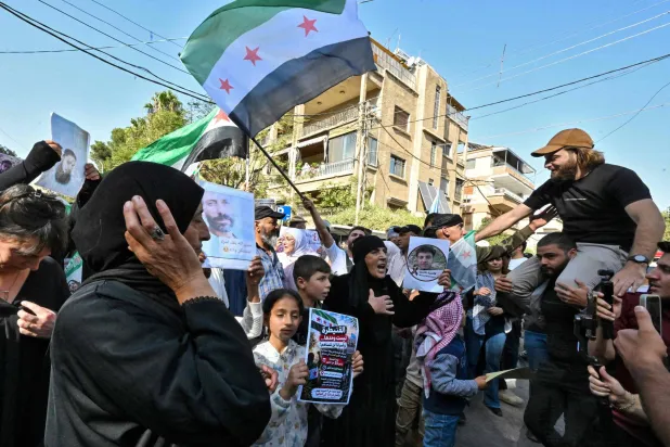 Syrians wave flags and hold portraits of people who were arrested during Israeli military incursions in southern Syria, as they protest near the United Nations building in Damascus, on October 23, 2026. (AFP)