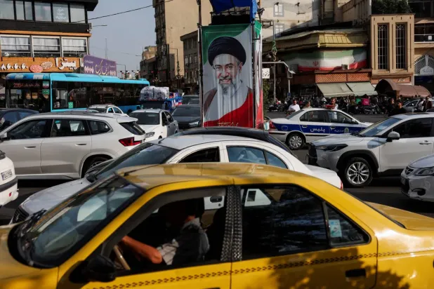 Tahran’da bir caddede İran Dini Lideri’nin resminin asılı olduğu bir tabelanın önünden araçlarıyla geçen insanlar (Reuters)