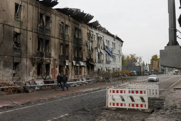 Rusya’nın 27 Ekim 2026 gecesi Kiev’e düzenlediği füze saldırısında hasar gören bir binanın önünden geçen bölge sakinleri (Reuters)