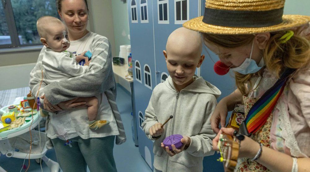 Tetiana Nosova, who goes by the clown name of Zhuzha, a volunteer from the "Bureau of Smiles and Support" plays a ukulele as she stands with Michael Bilyk, who is held by his mother Antonina Malyshko, and Kira Vertetska, 8, at Okhmatdyt children's hospital in Kyiv, Ukraine, Thursday Sept. 19, 2024. (AP Photo/Anton Shtuka)

