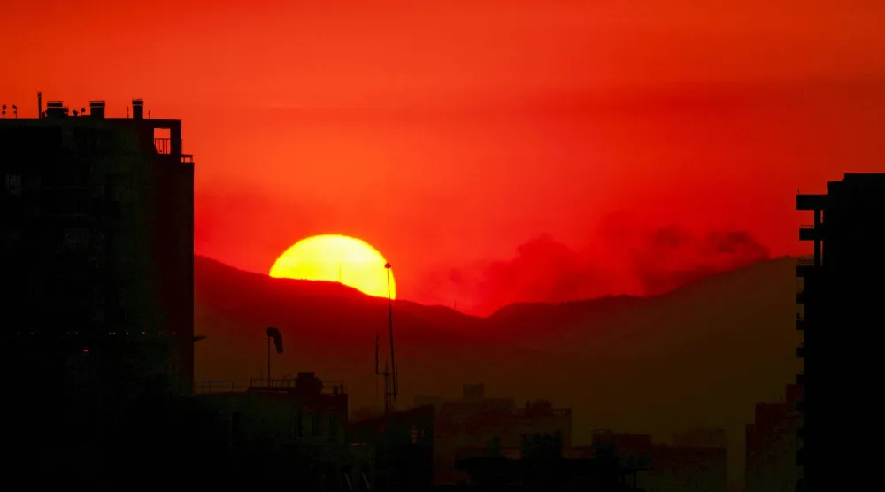 The sun sets in Santiago, Chile, Friday, Dec. 20, 2024, as a forest fires burns on the outskirts of the capital. (AP Photo/Esteban Felix)