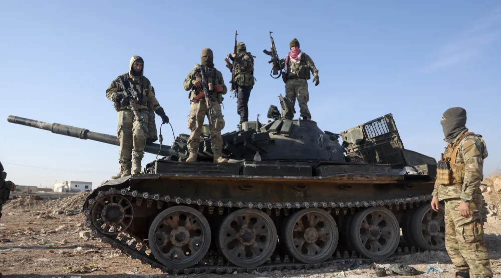 Syrian opposition fighters stand atop a seized military armored vehicle on the outskirts of Hama, Syria, Dec. 3, 2024. (AP Photo/Ghaith Alsayed)