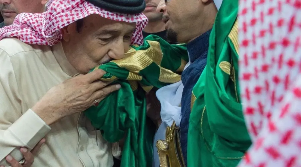الملك سلمان مقبّلاً العلم السعودي (واس)