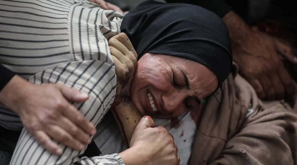 فلسطينية تبكي من الألم وهي تعانق أحد أحبائها الذي قُتل في هجمات إسرائيلية استهدفت منازل مؤقتة وخياماً في مستشفى الشفاء بمدينة غزة (د.ب.أ)
