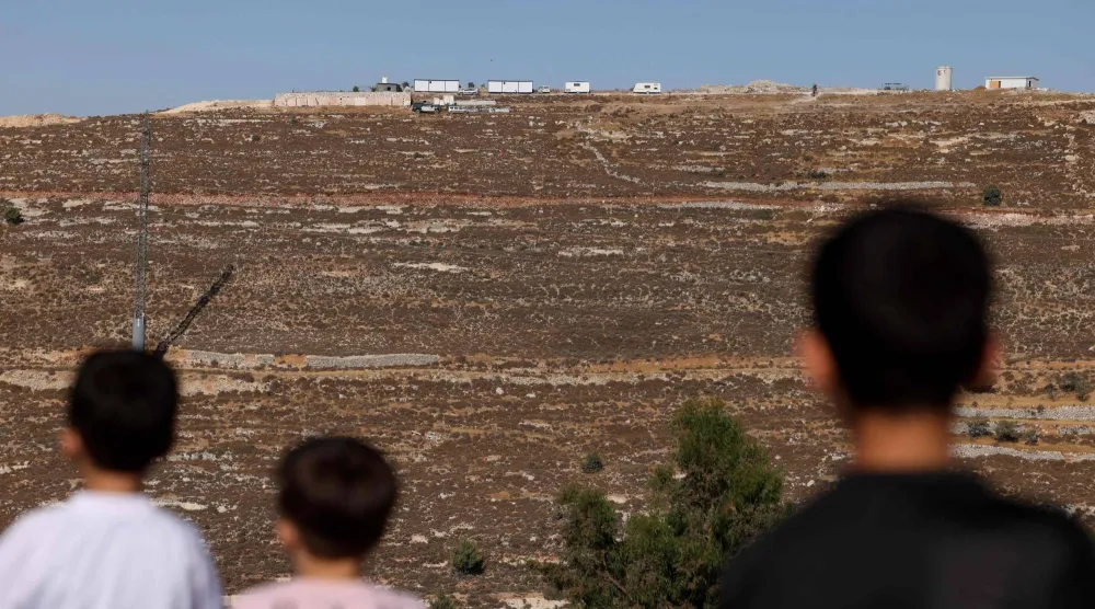أطفال فلسطينيون قبالة بؤرة استيطانية إسرائيلية جديدة اقيمت شمال الخليل في الضفة الغربية المحتلة، في 6 يوليو/تموز 2025 (أ ف ب)