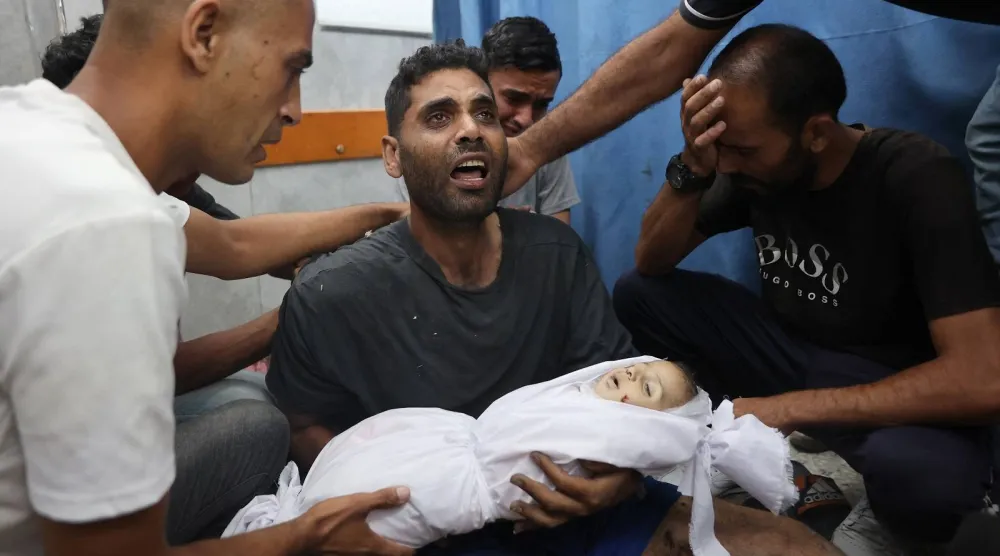 شاب فلسطيني يحمل جثمان ابنه الذي قُتل في غارة إسرائيلية جنوب غزة (أ.ف.ب)
