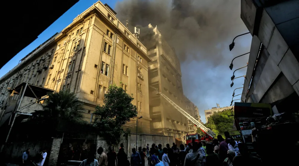 يراقب الناس رجال الإطفاء وهم يُخمدون ألسنة اللهب في حريق اندلع بمحطة تحويل الهواتف الأرضية ومبنى وزارة الاتصالات في قلب القاهرة (أ.ف.ب)