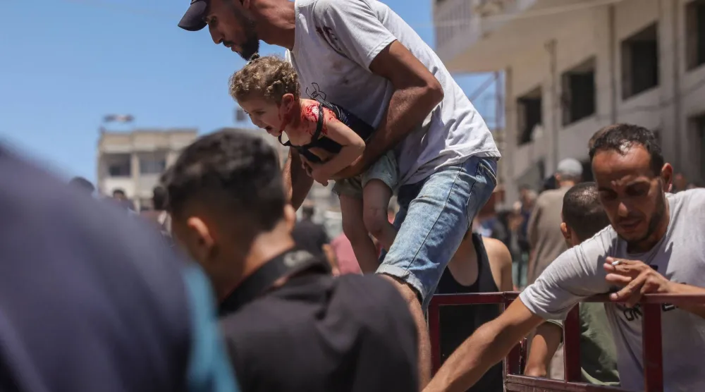 فلسطيني يحمل طفلة مصابة في موقع غارة إسرائيلية بجوار خيمة للنازحين في مدينة غزة يوم الثلاثاء (أ.ف.ب)