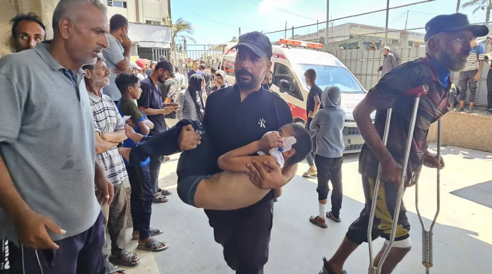 فلسطيني يحمل طفلاً مصاباً في غارة إسرائيلية على مخيم للنازحين قرب خان يونس (أ.ف.ب)