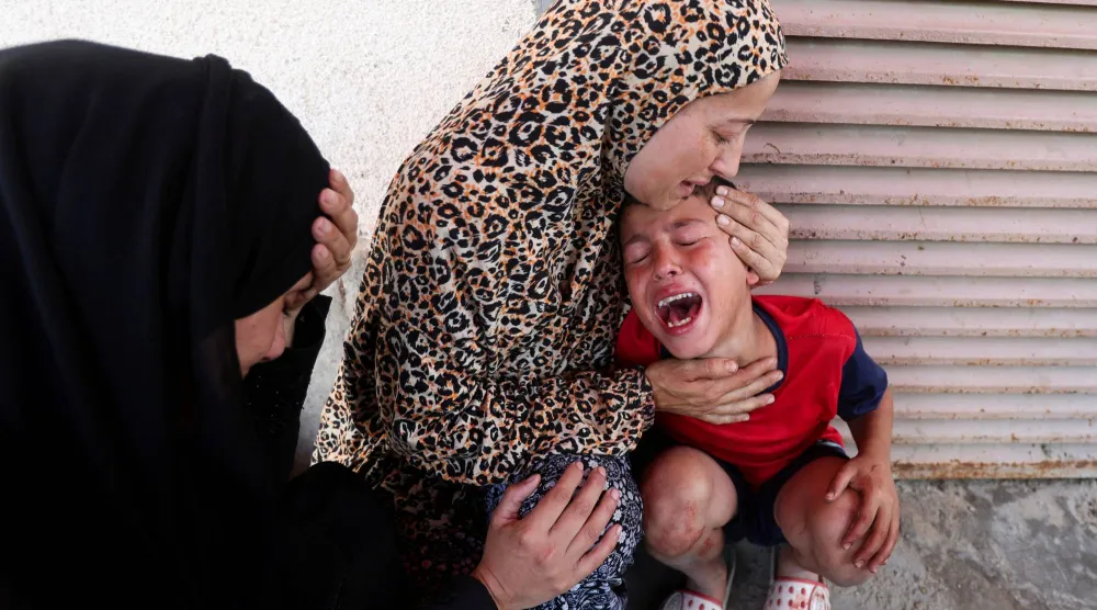 فلسطينية تهدّئ من روع طفل مع نقل ضحايا هجوم إسرائيلي إلى مستشفى في دير البلح يوم الخميس (رويترز)