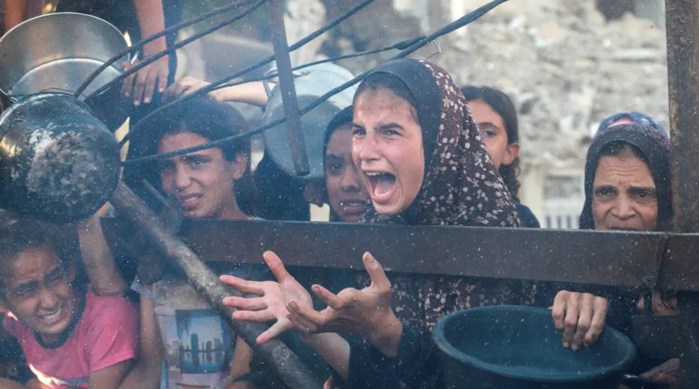 فتاة فلسطينية تتفاعل بينما تنتظر توزيع الطعام من مطبخ خيري وسط أزمة الجوع في مدينة غزة (رويترز)