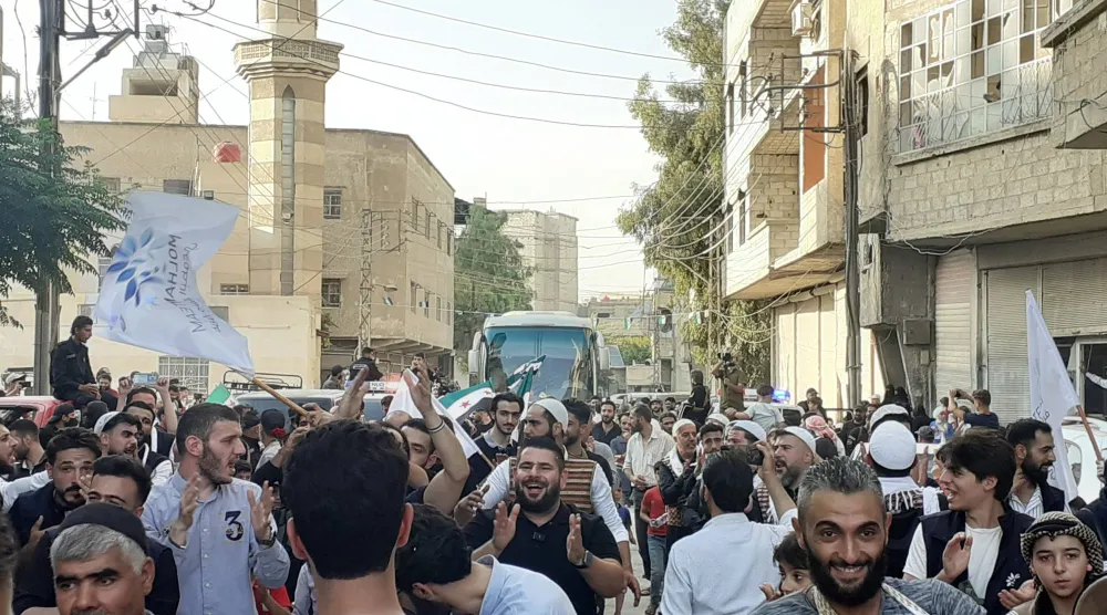 حشد المستقبِلين يحيط بحافلة تُقل عائدين في بلدة جسرين بغوطة دمشق الشرقية (الشرق الأوسط)