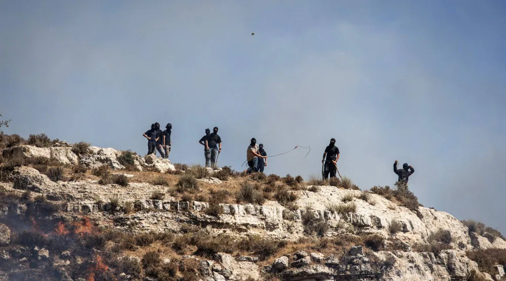 مستوطنون إسرائيليون ملثّمون يرشقون الفلسطينيين بالحجارة في بلدة سنجل بالضفة الغربية (أ.ف.ب)