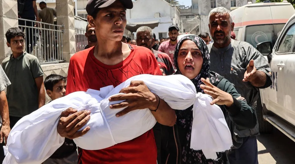 فلسطينية تسير بجوار شاب يحمل جثمان طفلها الذي قُتل في غارة إسرائيلية أمام مستشفى المعمداني (أ.ف.ب)
