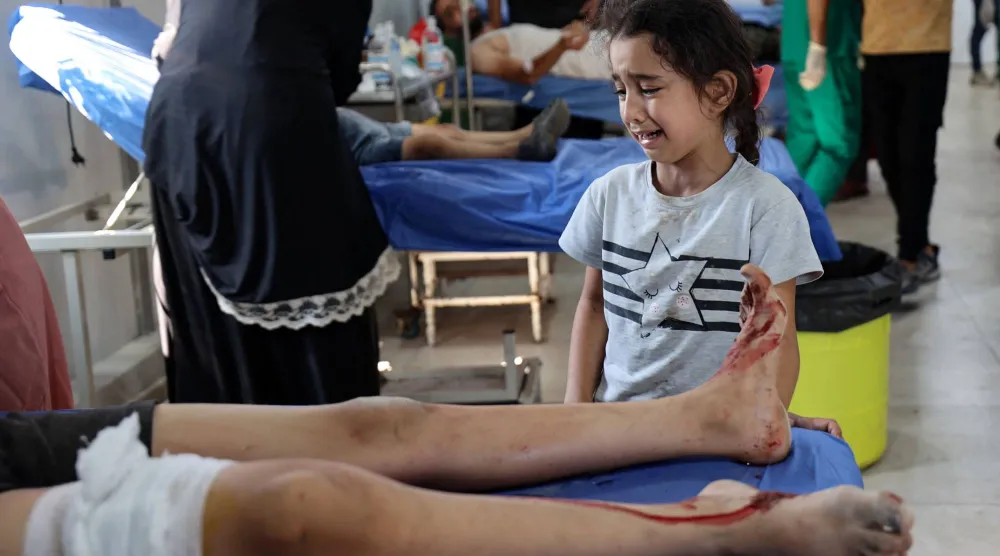 طفلة فلسطينية تبكي قرب طفل يتلقى العلاج من إصاباته في مستشفى العودة بالنصيرات وسط غزة الأحد (أ.ف.ب)