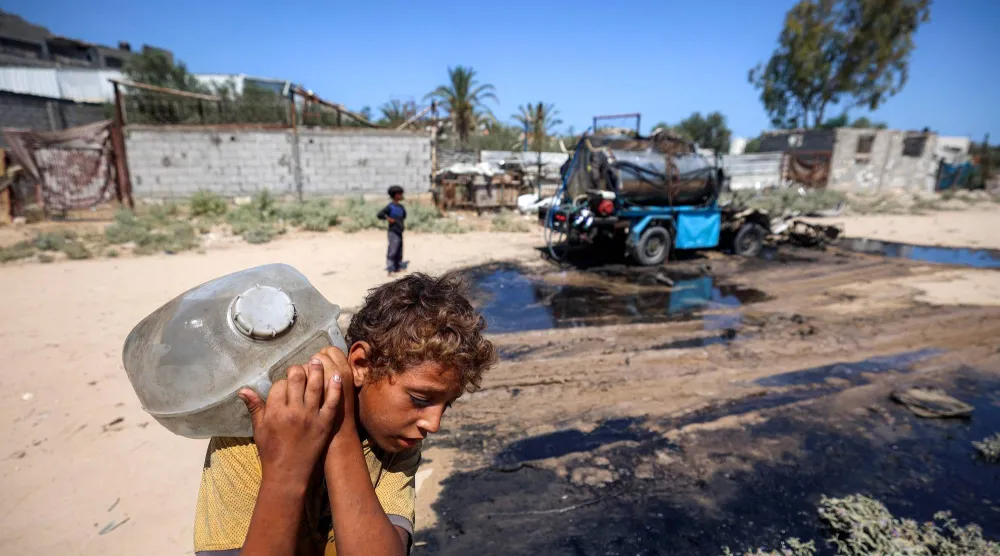 طفل فلسطيني يحمل وعاءً به مياه بعد ملئه من صهريج في مخيم النصيرات بقطاع غزة (أ.ف.ب)
