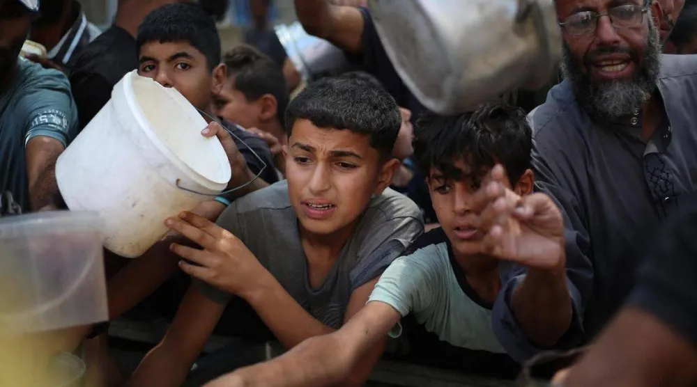 أطفال فلسطينيون يصطفون للحصول على حصة من الطعام الساخن الذي يوزعه مطبخ خيري في مخيم النصيرات للاجئين وسط غزة (أ.ف.ب)