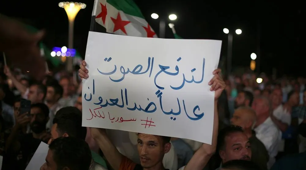A man holds a placard reading in Arabic "let us raise our voices against the aggression" during a protest against Israeli airstrikes in southern Syria, in Aleppo, Syria, 15 July 2025. (EPA)