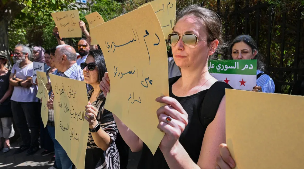 سوريون يرفعون لافتات خلال مظاهرة احتجاجية على الاشتباكات والضربات الإسرائيلية في السويداء أمام البرلمان في دمشق (أ.ف.ب)