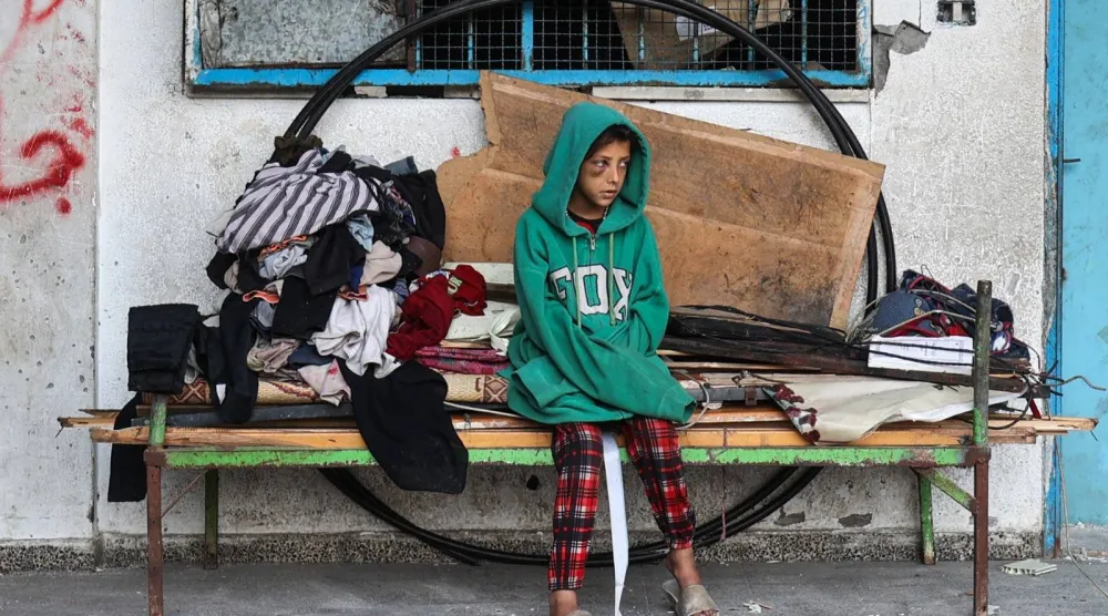 فتاة فلسطينية تنظر إلى الآخرين وهم يزيلون الحطام من مخيم مؤقت للنازحين تعرض لقصف إسرائيلي في مخيم البريج للاجئين (أ.ف.ب)