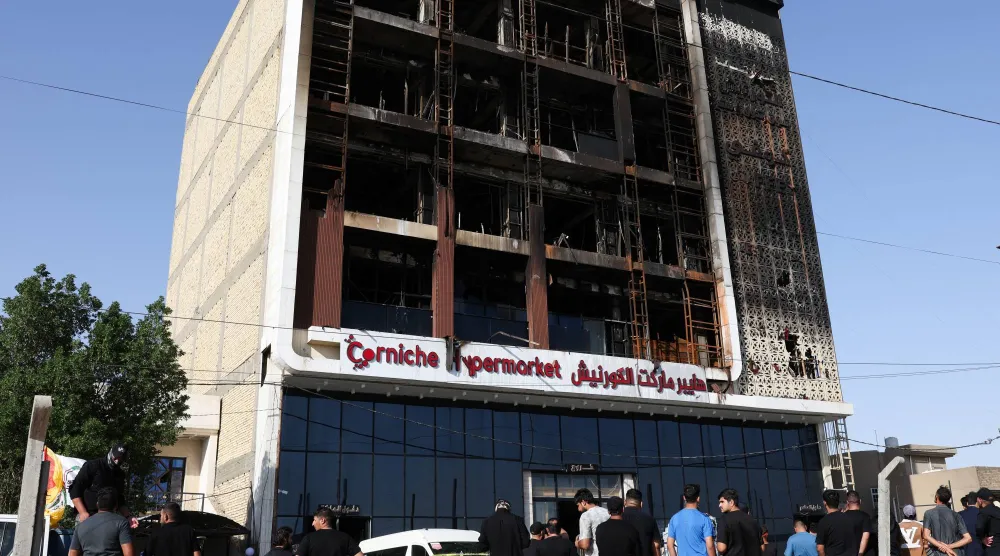 أشخاص يتجمعون بجوار مركز تجاري دمر خلال حريق هائل اندلع ليلاً وأودى بحياة العشرات في الكوت بمحافظة واسط بالعراق (رويترز)