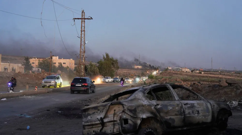 Smoke rises as a damaged car remains along a street, as Sweida province has been engulfed by nearly a week of violence, at Sweida governorate, Syria, July 18, 2025. REUTERS/Karam al-Masri
