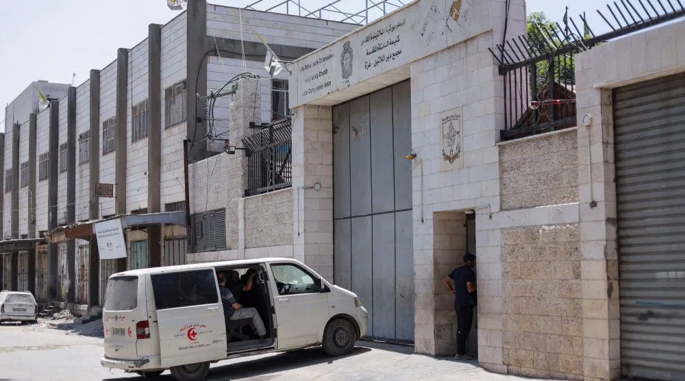 أشخاص يجلسون داخل مركبة أمام كنيسة العائلة المقدسة بغزة التي تضررت جراء قصف إسرائيلي (رويترز)