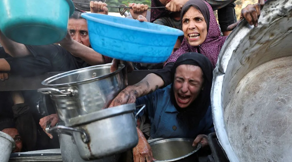 فلسطينيون يصرخون أثناء طلب الطعام من مطبخ خيري وسط أزمة الجوع في غزة (رويترز)