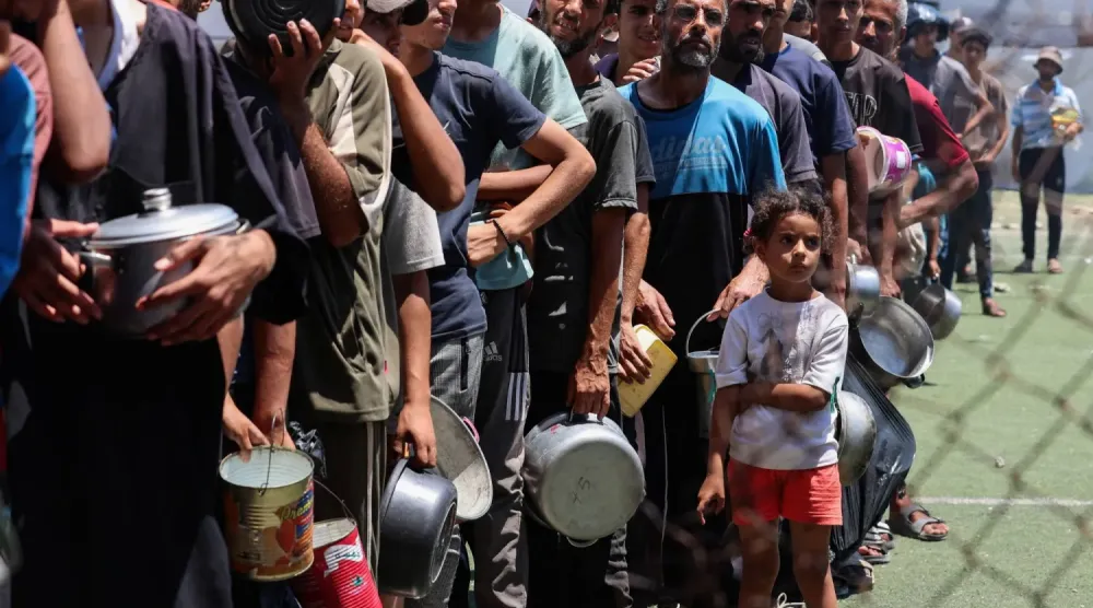 Filistinliler Gazze Şeridi'nin orta kesimindeki Nuseyrat'ta açlık krizinin ortasında bir yardım mutfağından yiyecek almak için toplanıyor (Reuters)