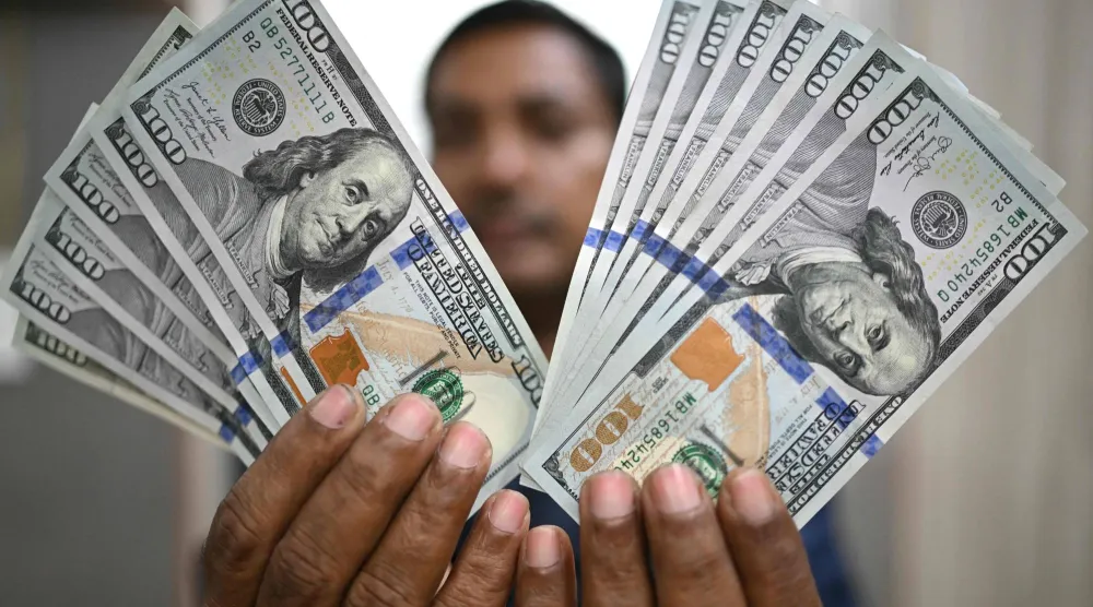 رجل يمسك أوراقاً نقدية من فئة 100 دولار في محل صرافة بالعاصمة الهندية نيودلهي (أ.ف.ب)