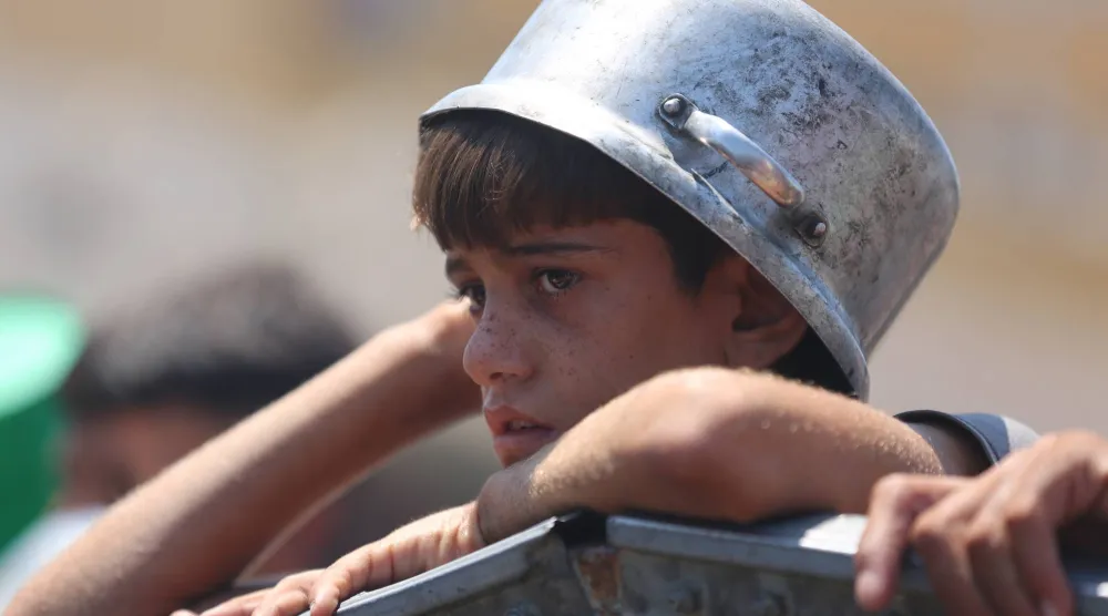 في انتظار الطعام ... طفل فلسطيني يضع قدره على رأسه أمام مطبخ خيري في غزة أمس (د.ب.أ)