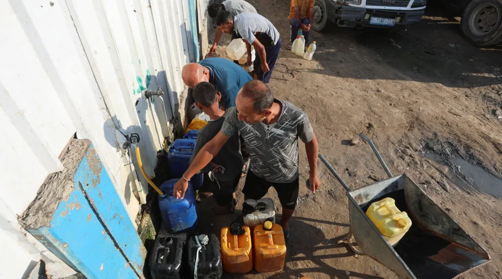 فلسطينيون يملأون أوعية بالماء من مركز توزيع في دير البلح بوسط غزة الثلاثاء (رويترز)