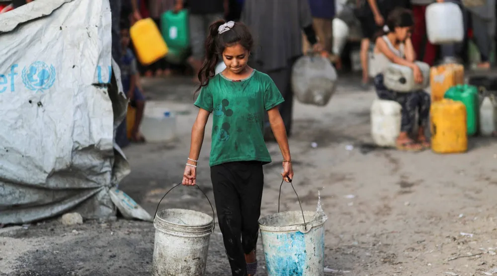 فتاة فلسطينية تحمل دلاء من الماء وسط نقص في المياه في مدينة غزة (رويترز)